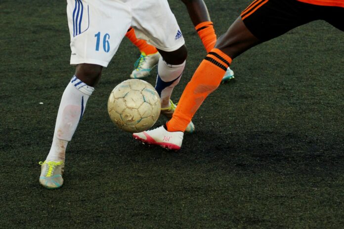 Two football players challenge for the ball during a match on an artificial pitch, highlighting youth competition and intensity.