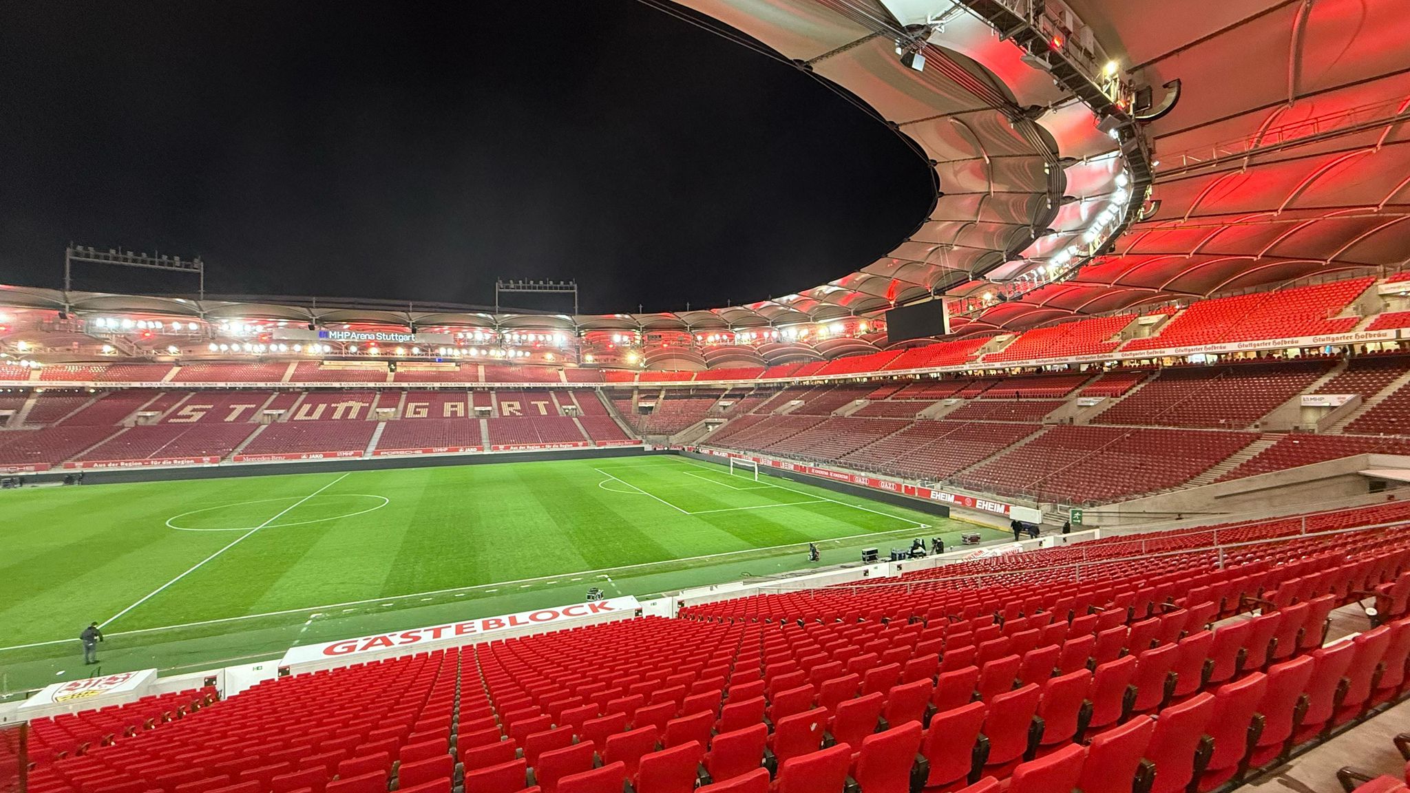View of the empty MHP Arena in Stuttgart at night, with red stadium lights illuminating the seating and pitch before a match.