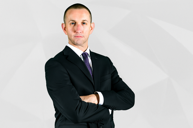 David Platt in a black suit with arms crossed, posing confidently against a light geometric background