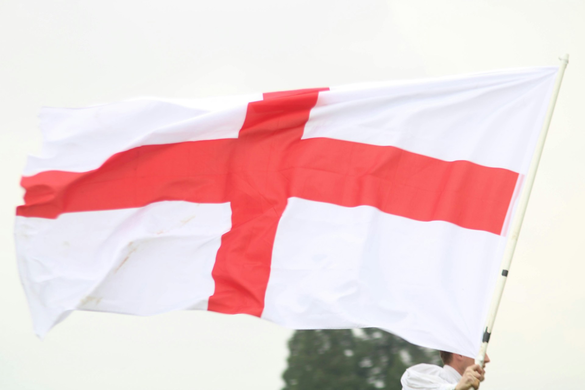 A person waves a large England flag featuring the red cross of St George, symbolizing national pride and support for England's football team.