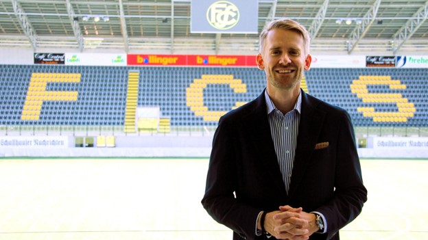 Jan Wappler standing in front of the FC Schaffhausen stadium stands, smiling in a suit