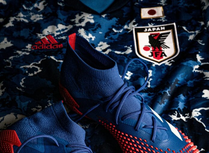 Close-up of blue and red Adidas football boots placed on the Japanese national team jersey, featuring the JFA (Japan Football Association) crest.