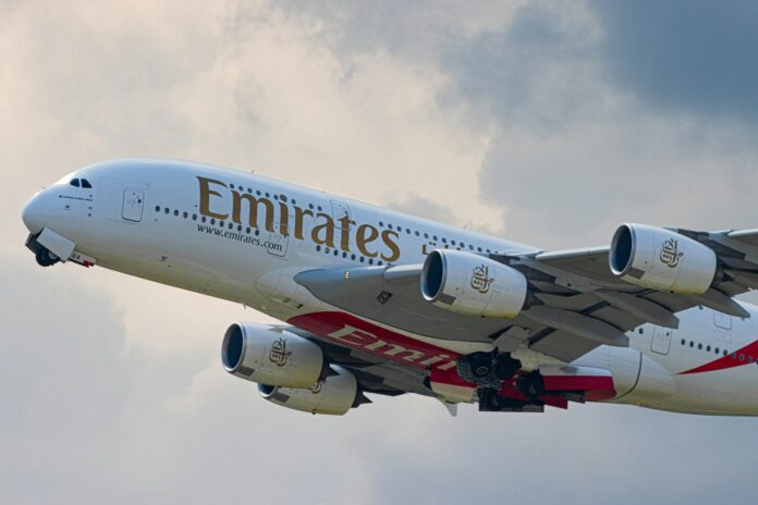 An Emirates Airbus A380 aircraft taking off, with its landing gear retracting and engines visible against a cloudy sky.