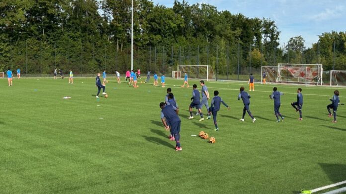 Young football players in training on a green pitch, practicing warm-up drills under coach supervision.