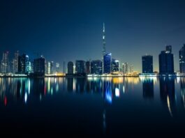 Why Dubai Developers Target Premier League Clubs Dubai skyline at night with illuminated skyscrapers reflected on the water, representing the city’s booming real estate market and global investment appeal.