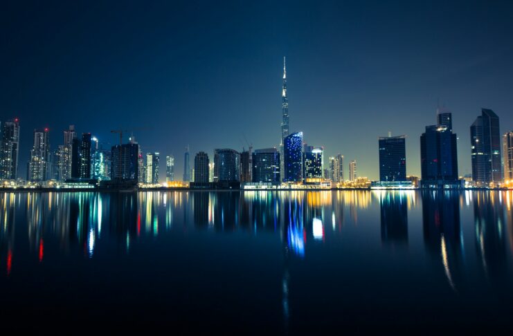 Dubai skyline at night with illuminated skyscrapers reflected on the water, representing the city’s booming real estate market and global investment appeal.