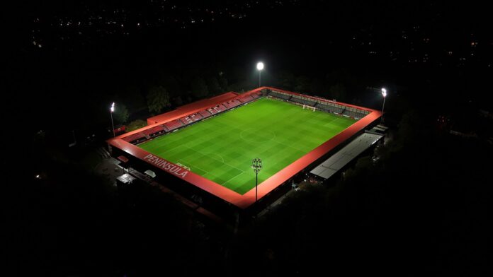 Aerial night view of The Peninsula Stadium in Salford, symbolizing the connection between football, business, and community value.