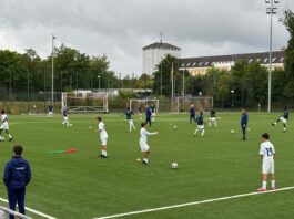 Youth players train in structured drills demonstrating coordinated movement, spacing and defensive principles on a modern football training pitch.