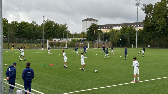 Youth players train in structured drills demonstrating coordinated movement, spacing and defensive principles on a modern football training pitch.
