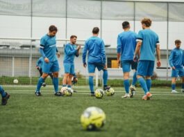 Football players in blue training kits practicing tactical drills on a synthetic pitch.