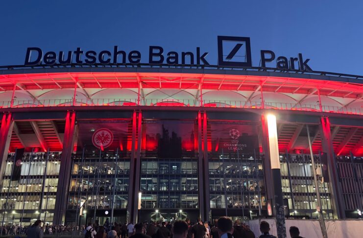 Deutsche Bank Park stadium lit in red at night showcasing prominent naming rights branding above the main entrance.