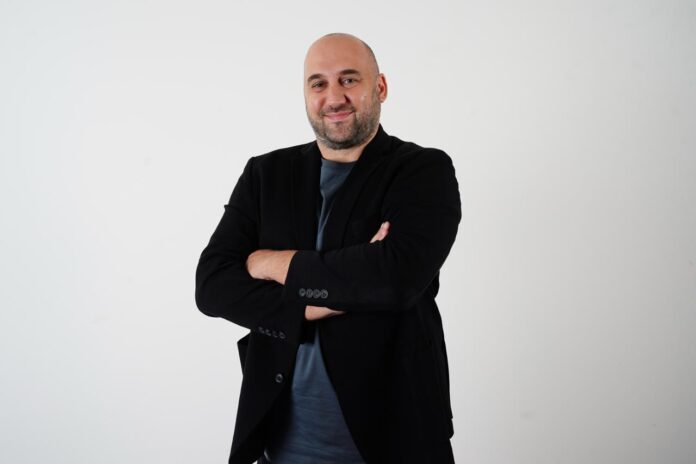 Emir Güney stands with arms crossed, reflecting leadership and expertise in sports education and football governance.