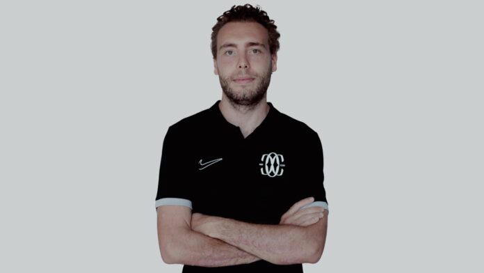 Gianni Piccatti standing with folded arms in a black Como Women polo during his profile interview for The Football Week.