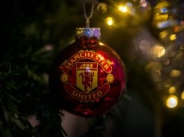 Manchester United Christmas ornament hanging on a tree with festive lights in the background.