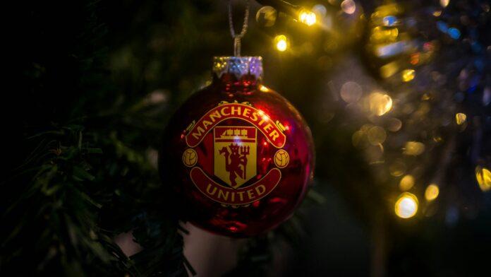 Manchester United Christmas ornament hanging on a tree with festive lights in the background.