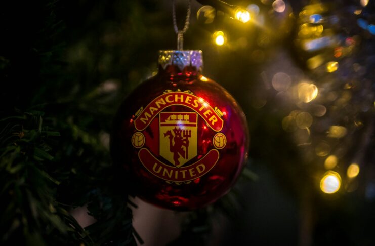 Manchester United Christmas ornament hanging on a tree with festive lights in the background.