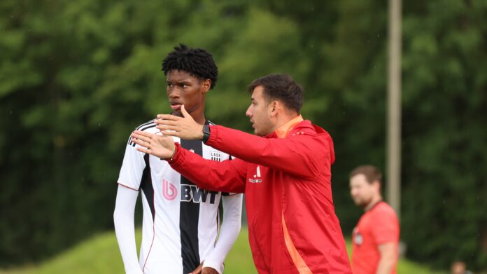 Coach giving tactical instructions to a young player during a training session for LASK, emphasizing positioning and movement.