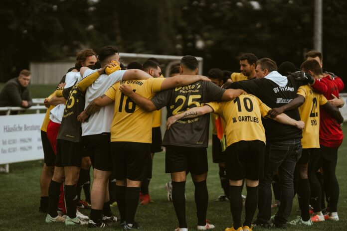 Football team huddle before kick off, players linked arm in arm to build focus, unity, and collective mindset on the pitch.