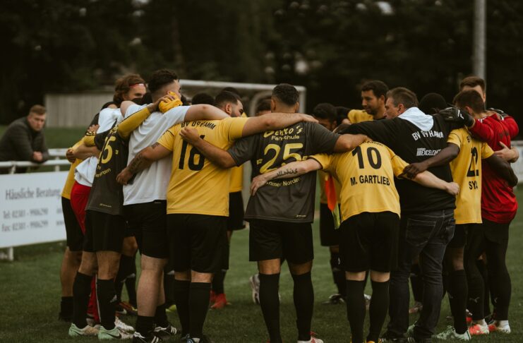 Football team huddle before kick off, players linked arm in arm to build focus, unity, and collective mindset on the pitch.