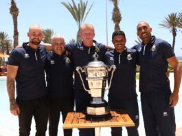 Yohwen Guihard with coaching team posing by the poolside with the league trophy.