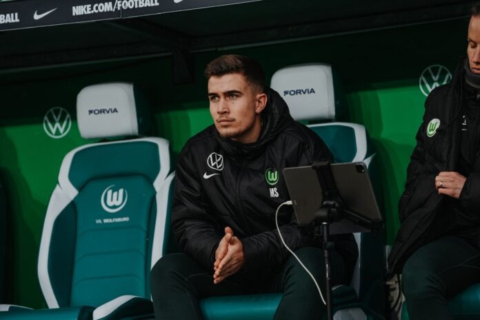 Marcel Schulz seated on the VfL Wolfsburg bench during a Frauen-Bundesliga match, focused and analysing play.
