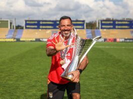 André Vale celebrates with a trophy on the pitch, highlighting his leadership journey in elite football coaching.