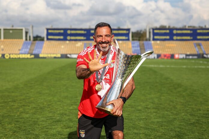 André Vale celebrates with a trophy on the pitch, highlighting his leadership journey in elite football coaching.