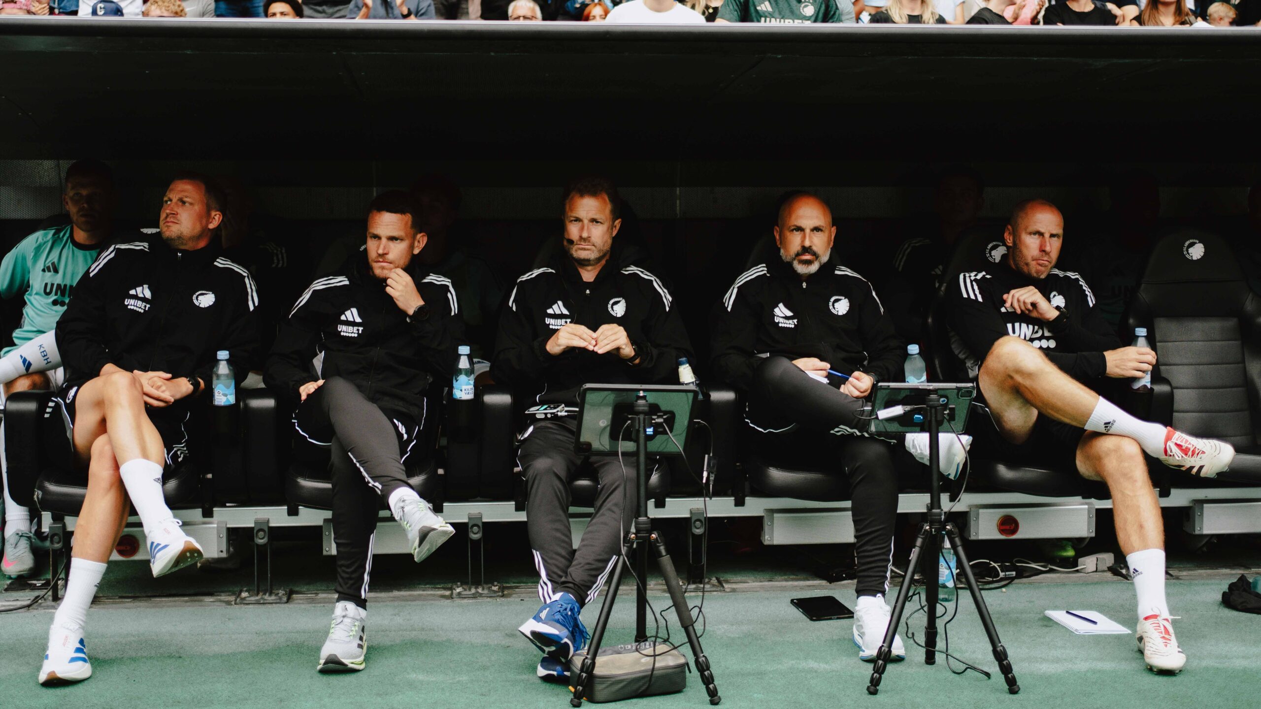 Sergio Almenara seated on the bench with coaching staff during a match, highlighting collaboration and match preparation.