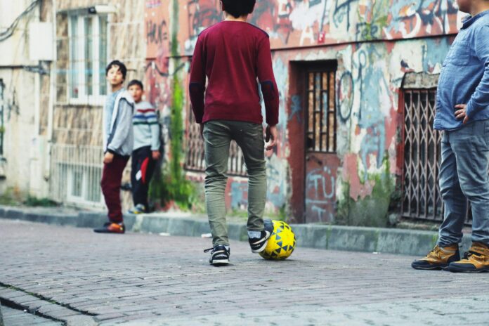 Children playing street football in an urban setting, reflecting grassroots engagement and community impact in the football ecosystem.