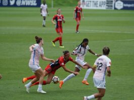 Women’s footballers contest possession during a match, highlighting professionalism and the pay gap discussed in the article.
